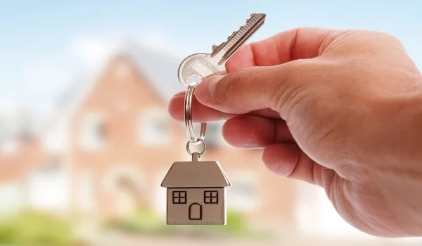 Hand holding a house-shaped keyring in front of a completed home
